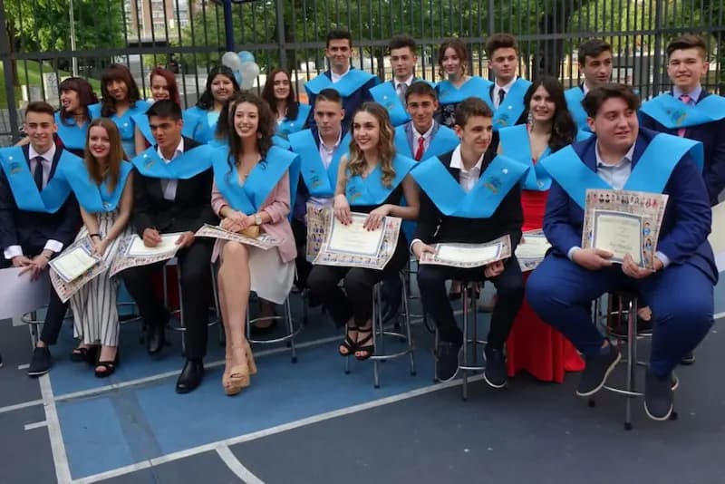Alumnado de graduación con beca azul y diploma, sentado en fila en la pista del colegio.