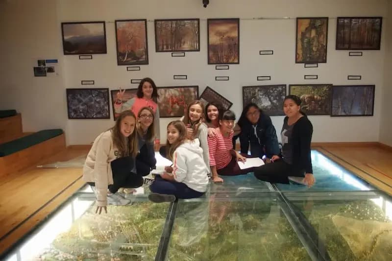 Alumnas y alumnos de Secundaria agrupados sobre el suelo de cristal de una exposición, con fotografías de paisajes en las paredes.